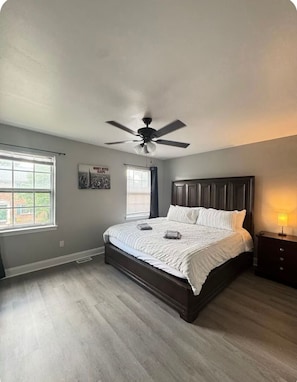 A bedroom with a bed, a ceiling fan, a window, and a nightstand.