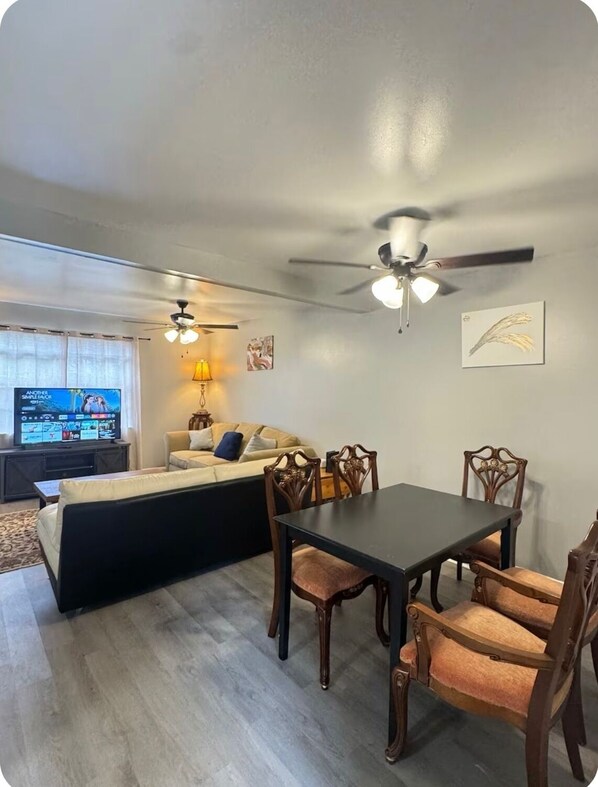 A living room with a sofa, a TV, a ceiling fan, and a dining table with chairs.
