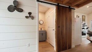 A room with a wooden floor, a sliding barn door, a kitchen with white cabinets, and a dining area with a table and chairs.