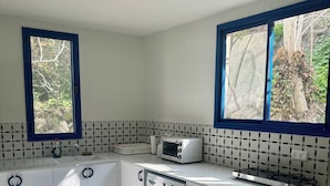 Eine moderne Küche mit integriertem Waschtrockner, Mikrowelle und Toaster. Zwei Fenster sorgen für natürliches Licht und bieten Blick ins Grüne.