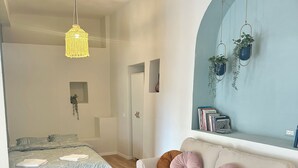 Ein modernes Schlafzimmer mit einem Bett, einer Couch, einer hängenden Pflanze und einem Bücherregal.