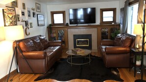 A living room with leather sofas, a flat-screen TV, a fireplace, and a wooden floor. - Spacious Sugarhouse Bungalow close to downtown and the canyons! (Salt Lake City)