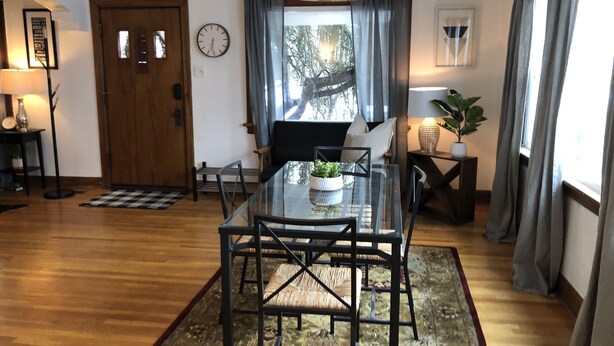 A dining area with a glass table, chairs, a chandelier, a clock, and a window with curtains. - Spacious Sugarhouse Bungalow close to downtown and the canyons! (Salt Lake City)