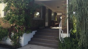 A two-story house with a covered porch, brick exterior, and a staircase leading to the entrance. - Spacious Sugarhouse Bungalow close to downtown and the canyons! (Salt Lake City)