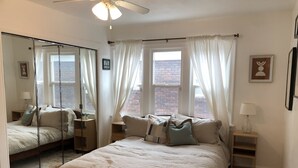 A bedroom with a large bed, a bedside table, a mirror, and a window with curtains. - Spacious Sugarhouse Bungalow close to downtown and the canyons! (Salt Lake City)