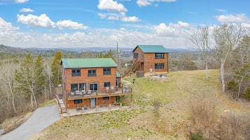 Une cabane en bois à deux étages, dotée d’un toit végétalisé, d’un balcon et d’un patio aménagé avec des sièges d’extérieur.