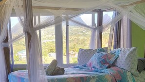 A bed with a canopy, a view of the outdoors, and a green wall. - Majestic views  of Pitons, Caribbean sea, amazing sunsets right from your room (Choiseul)