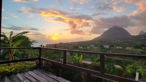 A wooden deck with a view of a sunset over a mountain and a village. - Majestic views  of Pitons, Caribbean sea, amazing sunsets right from your room (Choiseul)