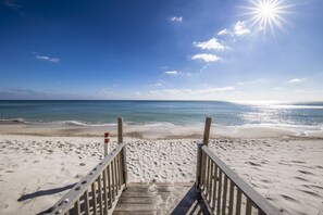 A wooden boardwalk leading to a beach with a clear sky and sun shining.
