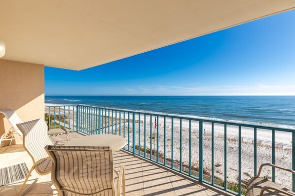 A balcony with a view of the ocean, equipped with wicker chairs and a table.