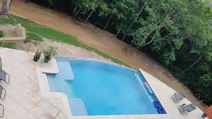 Ein rechteckiger Swimmingpool mit einer gefliesten Liegefläche, umgeben von einer Rasenfläche und Bäumen.