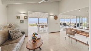 A spacious living area with a sofa, a wooden coffee table, and a seahorse decoration. There is a dining area with chairs and a table, and a large window offering a view of the ocean. - Villa blue Oasis, Coral Estate, Curacao (Willemstad, Curacao, Curacao, Caribbean)