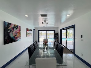 Un espace repas moderne avec une table en verre, des chaises noires et des œuvres d’art accrochées aux murs.