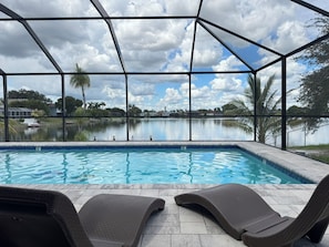 Une piscine intérieure avec deux chaises longues, une vue sur un lac et un ciel nuageux.