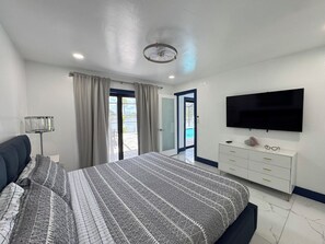 Un dormitorio con cama, televisor, cómoda y vista al exterior.