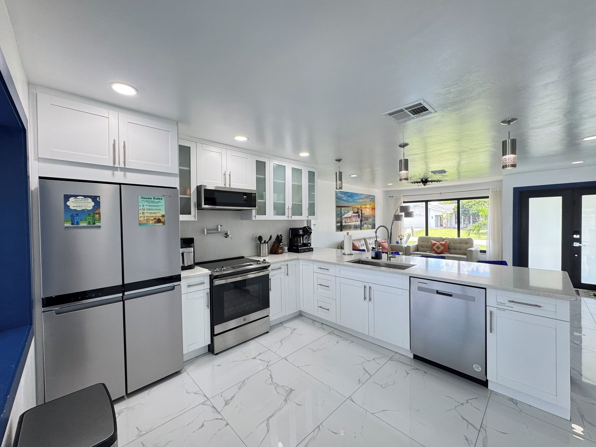 A modern kitchen with stainless steel appliances, white cabinetry, and a large window offering a view of the outdoors.