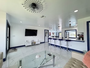 A modern kitchen with a bar area, a flat-screen TV, and a glass coffee table. - Lakefront home with heated pool & kayaks (Cape Coral)