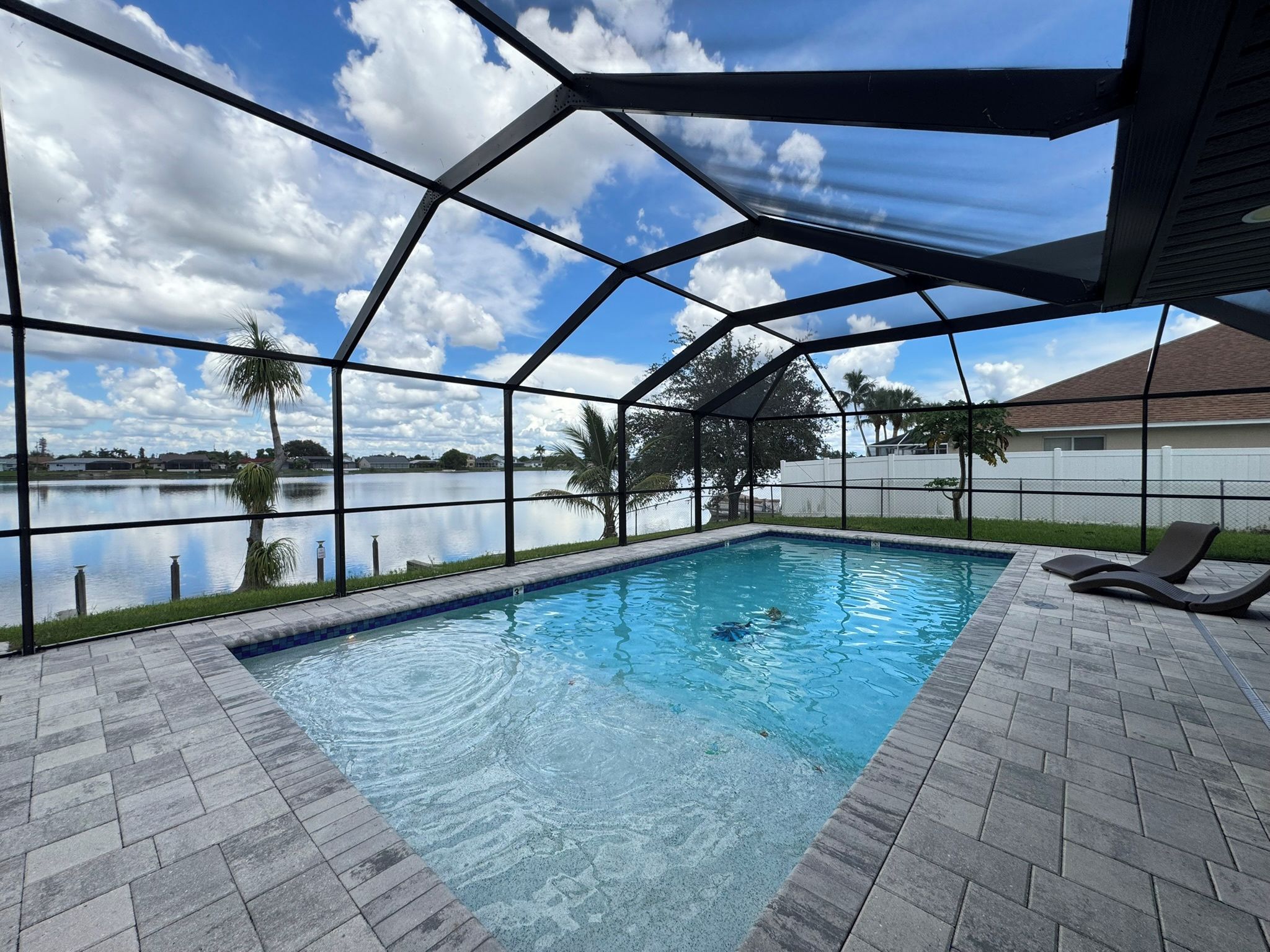 A swimming pool with a view of a lake and palm trees, surrounded by a covered patio area.