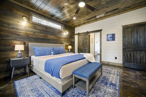 Un dormitorio con techo de madera, una cama grande con ropa de cama azul, un banco y una alfombra estampada.