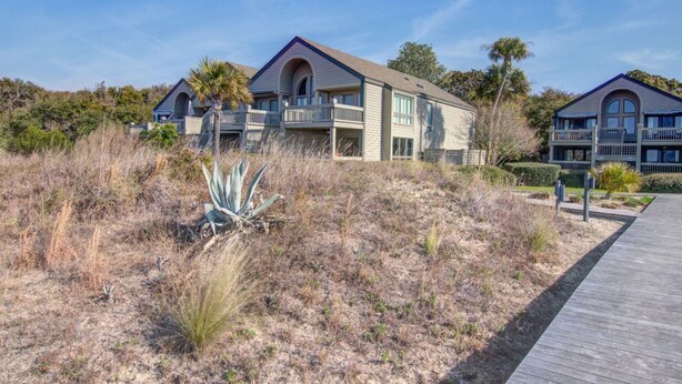 A beachfront property with a wooden boardwalk leading to a building with multiple balconies and a large window. - Seabrook Exclusives | 1397 Pelican Watch (Seabrook Island)