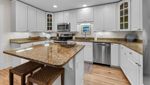 Eine moderne Küche mit weißen Schränken, Granit Arbeitsplatten, Edelstahlgeräten und einer integrierten Kücheninsel mit Hockern.