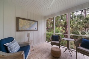 A room with a large window, a map on the wall, a blue sofa, wicker chairs, and a small round ottoman. - Kiawah Exclusives | 1031 Sparrow Cottage (Johns Island)