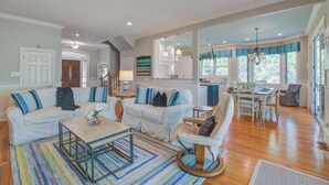 A spacious living room with a large sofa set, a dining area with a table and chairs, and a kitchen in the background. - Kiawah Exclusives | 65 Persimmon Court (Johns Island)