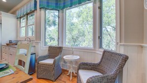 A cozy room with wicker chairs, a small round table, and a window with a view of trees. - Kiawah Exclusives | 65 Persimmon Court (Johns Island)