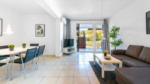 A modern living room with a dining area, a sofa, a TV, and a balcony with a view. - Casa Torremuelle I – 2-Bedroom Vacation Home with Pool, BBQ & Patio (Benalmádena)