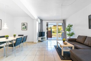 A modern living room with a dining area, a flat-screen TV, and a large sliding glass door leading to a balcony.