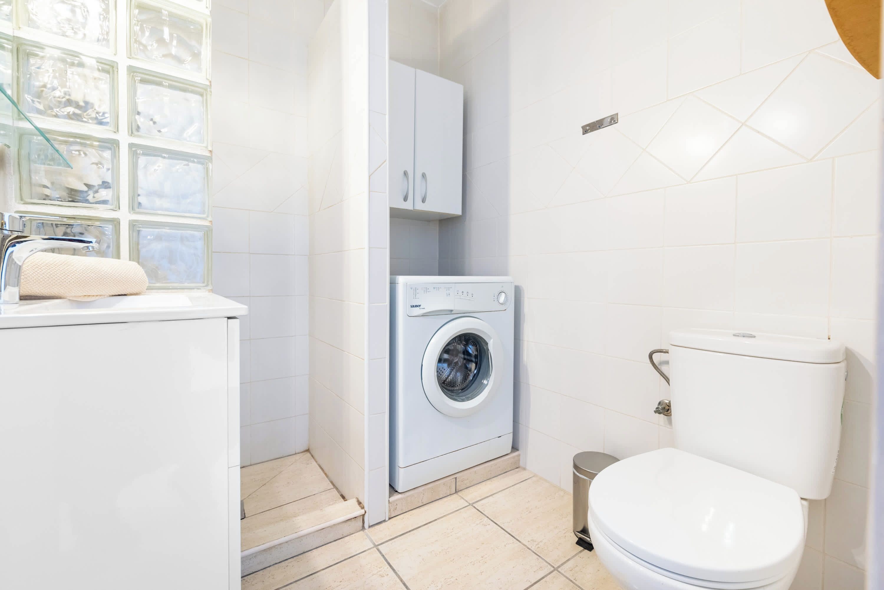 A compact bathroom with a washing machine, toilet, and a window with a towel on the counter.