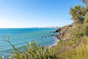 A coastal landscape with a clear view of the sea, a rocky shoreline, and a distant city skyline.