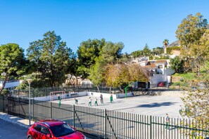 Una cancha de baloncesto rodeada por una valla, con árboles y edificios al fondo.