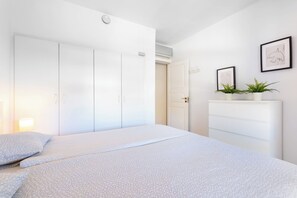 A bedroom with a bed, wardrobe, bedside table, and a potted plant.