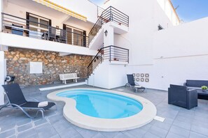 Una piscina con un muro de piedra y una escalera que lleva a un balcón.