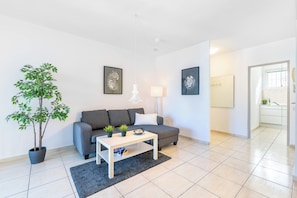 Una sala moderna con un sofá gris, una mesa de centro blanca y una planta grande en maceta.