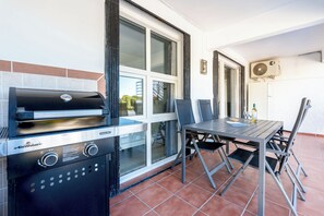 An outdoor patio with a grill, dining table, chairs, and a view of the street.