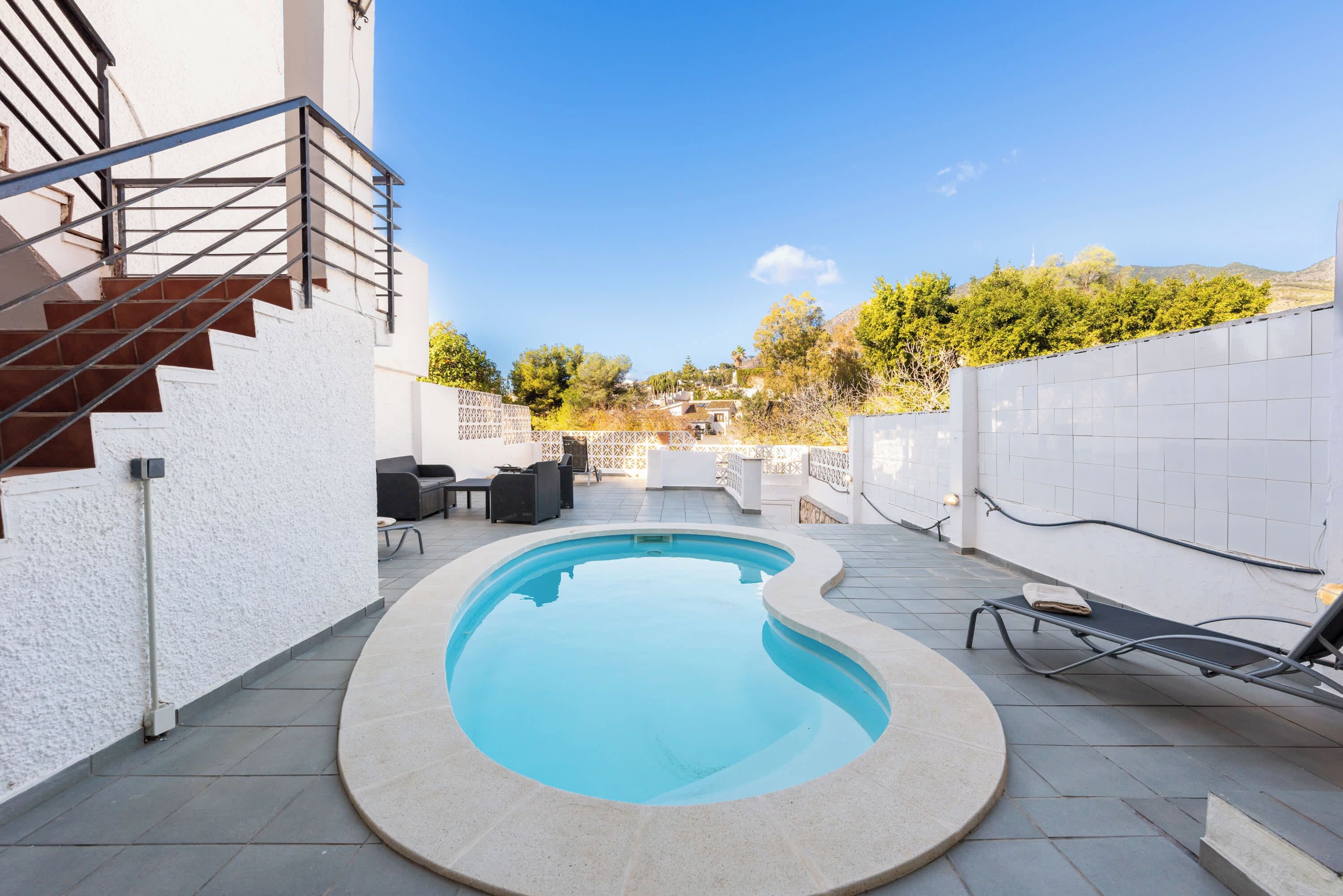 Une piscine à bordures courbes, entourée d’un mur blanc et d’une terrasse carrelée.