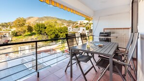 A balcony with a table and chairs, a grill, and a view of a town and hills. - Casa Torremuelle I – 2-Bedroom Vacation Home with Pool, BBQ & Patio (Benalmádena)
