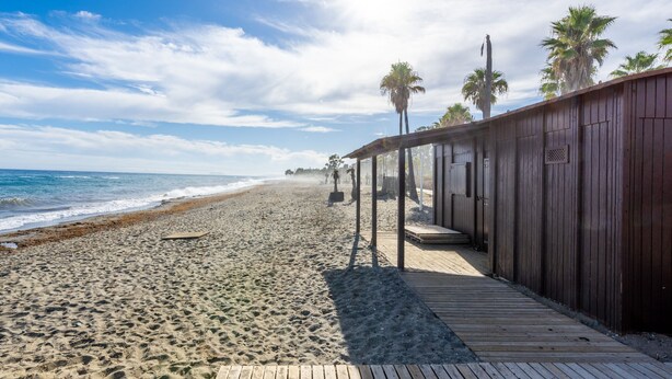 A wooden boardwalk leading to a beach with palm trees and a clear sky. - Casa Torremuelle I – 2-Bedroom Vacation Home with Pool, BBQ & Patio (Benalmádena)