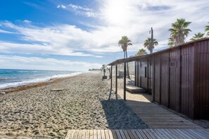 A wooden boardwalk leading to a beach with palm trees and a clear sky. - Casa Torremuelle I – 2-Bedroom Vacation Home with Pool, BBQ & Patio (Benalmádena)