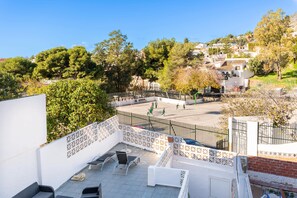 A rooftop terrace with outdoor seating, a basketball court, and a view of a hillside with buildings.