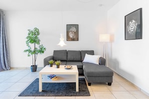 Una sala de estar moderna con un sofá gris, una mesa de centro blanca, una planta en maceta y dos cuadros en la pared.