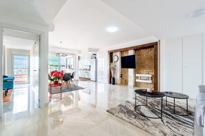 A spacious living area with a modern kitchen, a dining area with chairs and a table, and a large window offering a view. - La Nogalera Skyline | Stylish Apartment with Panoramic Sea Views & Pools in Torremolinos (Torremolinos)