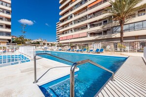 Un espace piscine d’hôtel avec une piscine à l’eau cristalline, des chaises longues et un palmier.