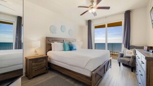 Ein Schlafzimmer mit einem großen Bett, einem Deckenventilator, einem Nachttisch, einer Kommode und Blick aufs Meer.