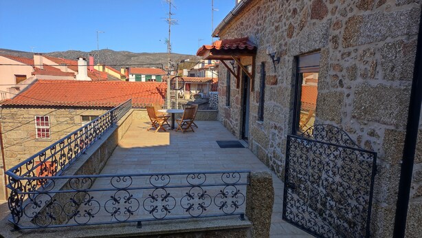 A stone building with a red-tiled roof, a balcony with metal railings, and a table with chairs. - Casa Cruz. (Trinta)