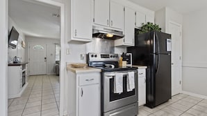 A modern kitchen with white cabinets, a stainless steel stove, and a black refrigerator. - Sandy Sands Retreat! Just 1 min to the beach! (Gulfport)