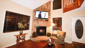 Una sala de estar con chimenea de piedra, un televisor montado encima y un sillón cómodo.