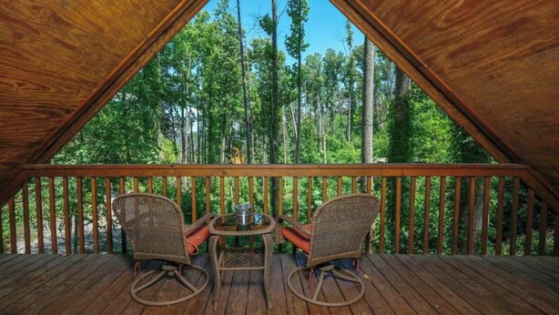 Una habitación tipo ático con terraza de madera, dos sillas de mimbre y una mesita.